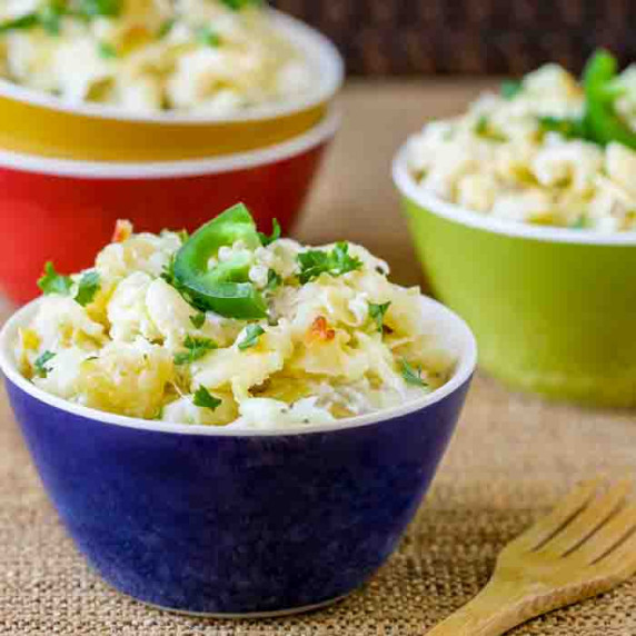 Side shot of three colorful bowls filled with Mac and cheese garnished with a slice of a jalapeno wi