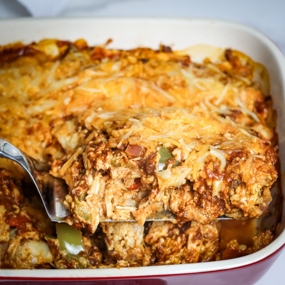 A serving of enchilada casserole being scooped out of the dish.