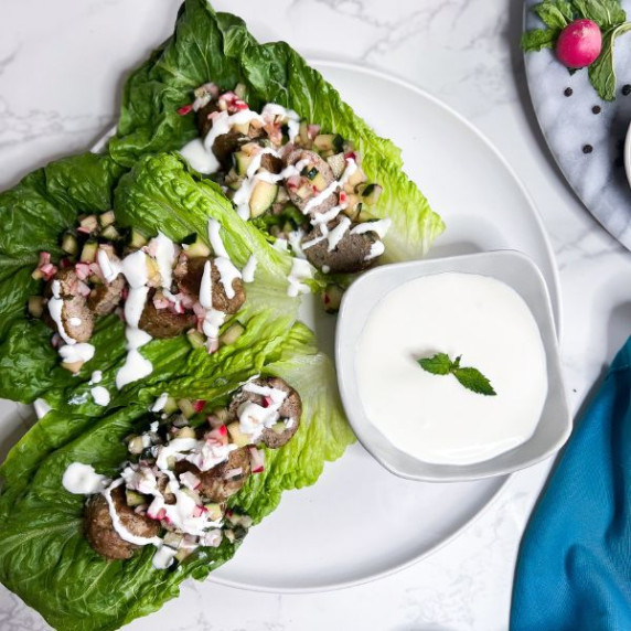 Lamb kofta wraps assembled on a white plate with feta-yogurt sauce in a bowl.