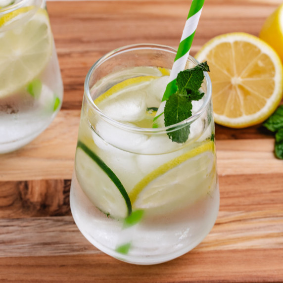 Lemon water with mint and cucumber in a glass with a green and white straw.