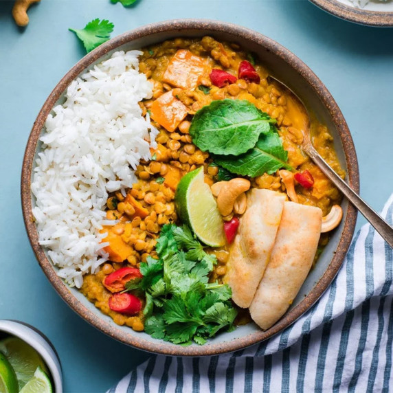 Bowl of lentil curry with naan and rice.