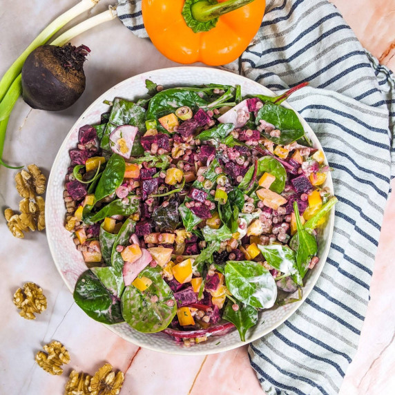 Pearl couscous and beetroot salad served in white bowl next to beetroot, green onions.