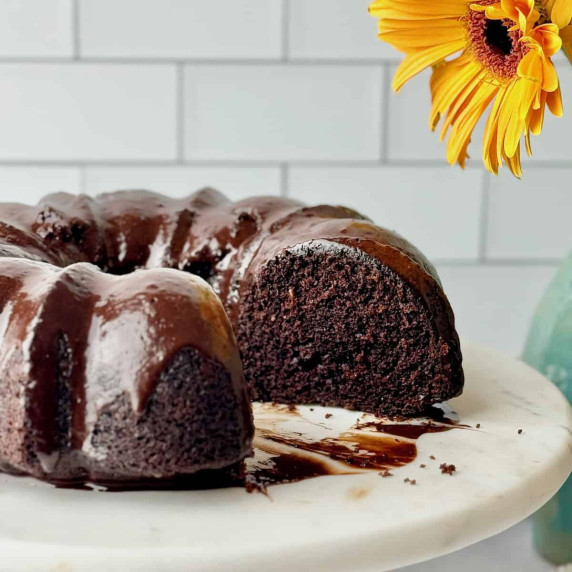 Chocolate cake on cake stand with a piece missing.
