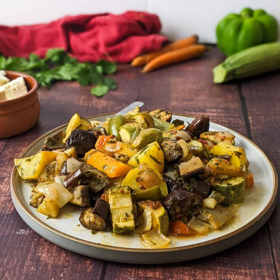 Briami casserole served on a plate next to raw vegetables and a bunch of parsley