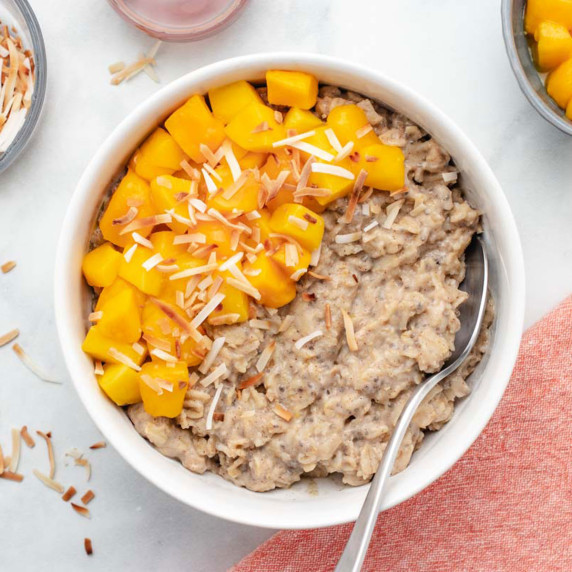Mango oatmeal with toasted shredded coconut in a white bowl with a spoon.