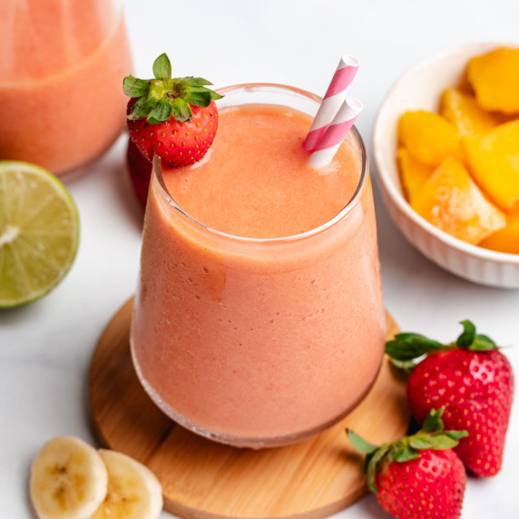 Mango, strawberry, and banana smoothie in a glass with a strawberry and two straws.