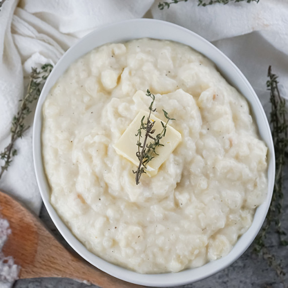 Overhead shot of mashed potatoes and parsnips with a pad of butter and herbs in a white bowl.
