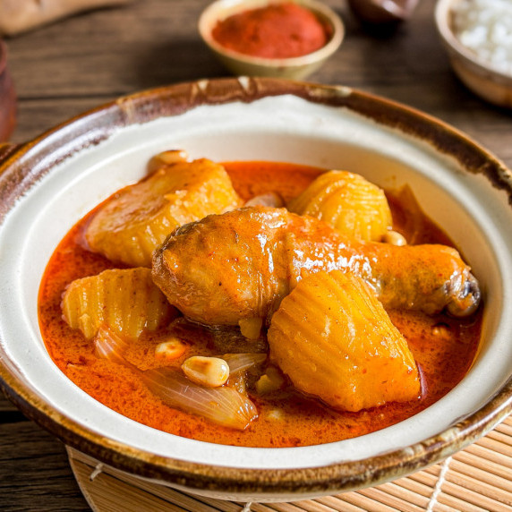 Close-up of massaman curry chicken with potatoes and peanuts in a clay bowl.