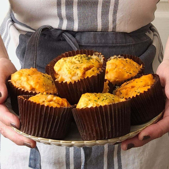 Close shot of woman with apron, holding out plate of cheesy muffins.
