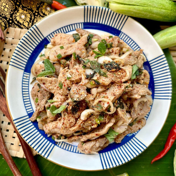 Top-view of nam tok moo, Thai grilled pork salad, garnished with fresh herbs and chilies.