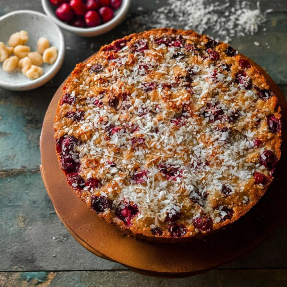 A festive Nantucket Cranberry Pie laid out on a wooden board with nuts and fresh cranberries.