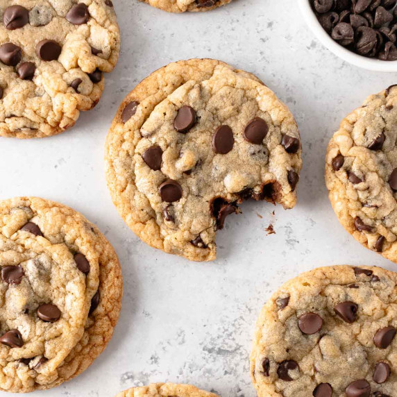 Classic chocolate chip cookies on a light surface, with one cookie bitten.