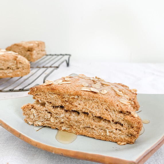 maple oat scone on a plate on a white tablecloth with maple syrup drizzle