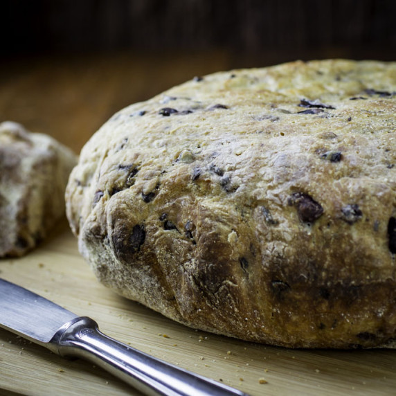 Close up shot of slow cooker olive parmesan bread on a wooden cutting board with a knife on the side