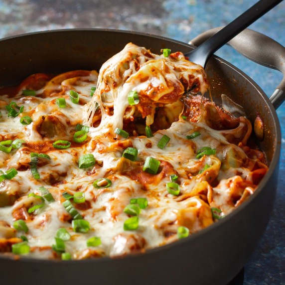 Side close up shot of a fork picking up a piece of cheese tortellini garnished with green onions. 