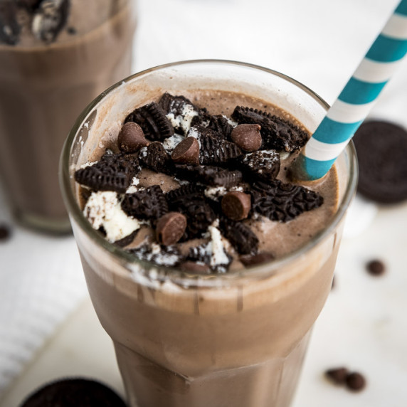 Angled close up shot of an oreo milkshake garnished with oreos and chocolate chips with a straw.