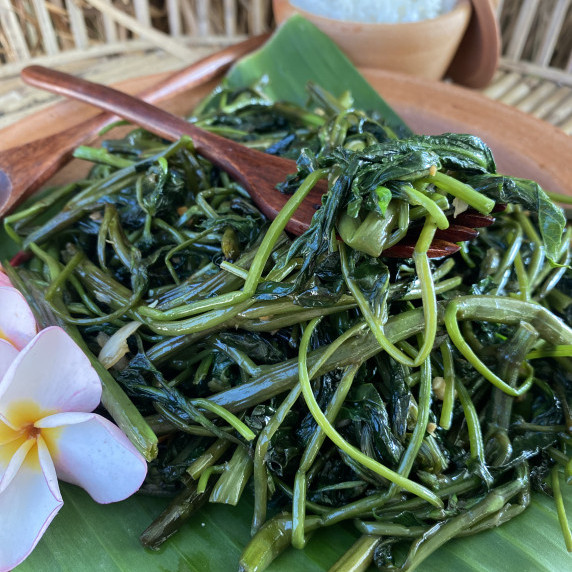 Stir-fried morning glory (pad pak boong) on a clay dish with a wooden fork on top.