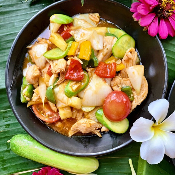 Top-down view of Thai sweet and sour chicken stir-fry with vegetables in a black dish.
