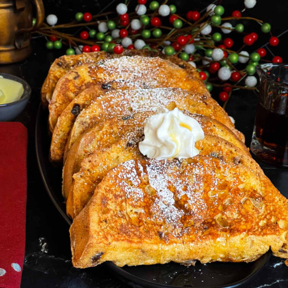 Panettone french toast garnished with powdered sugar and whipped cream stacked on a dark oval platte