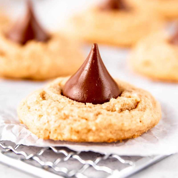 Close view of a four-ingredient peanut butter blossom cookie cooling on a parchment-lined wire rack.