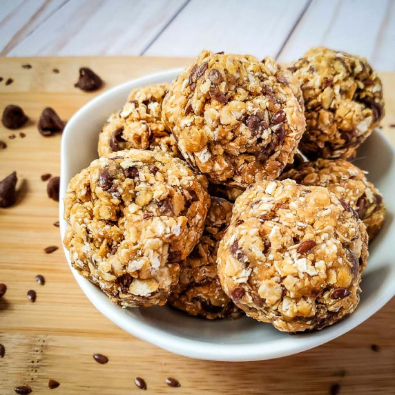 Side shot of multiple energy balls in a white bowl on a cutting board sprinkled with flax seeds and 