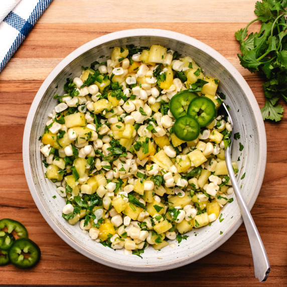 Pineapple corn salsa in a bowl with a spoon and sliced jalapeños.