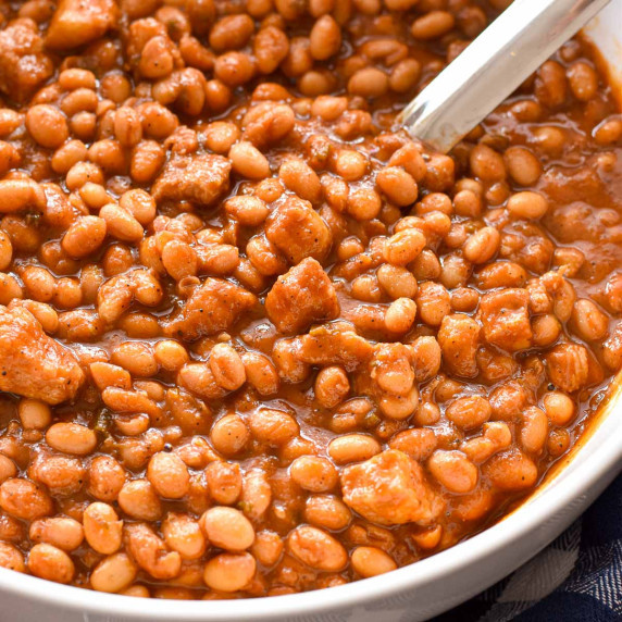 pork and beans in a white bowl with a spoon.