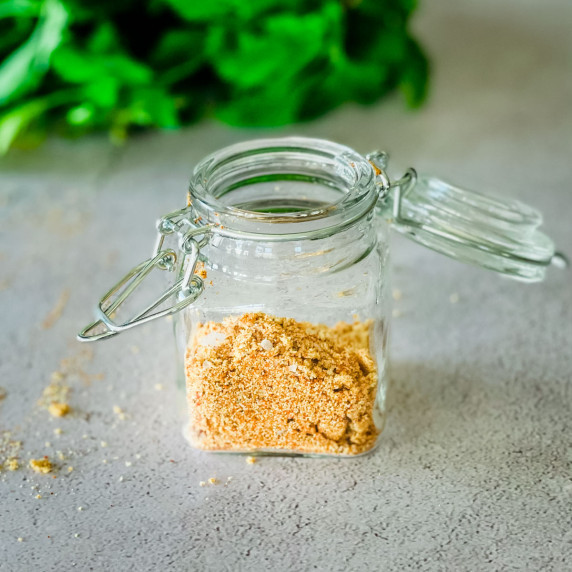 Homemade dry pork rub in a glass jar with green herbs in the background.