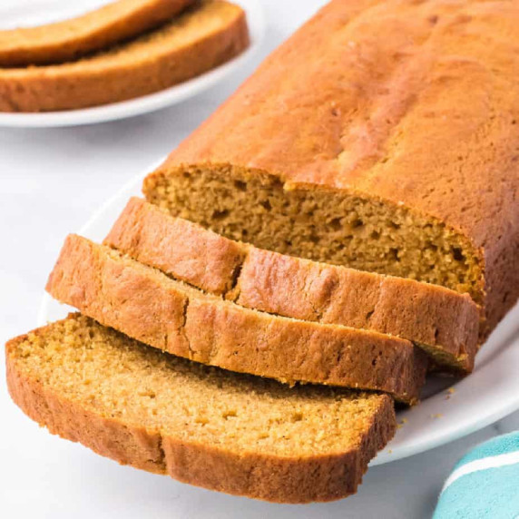 Sliced pumpkin loaf up on a plate on a counter with a plate of pumpkin bread slices behind.