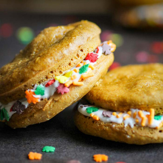 Side close up shot two whoopie pies leaning on each other on a grey surface with sprinkles in front.