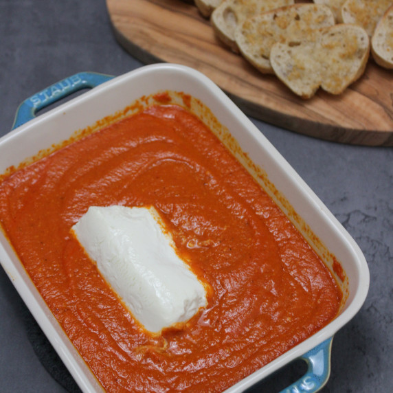 A dish of Spanish baked goat cheese in tomato sauce with garlic crostini on the side for dipping