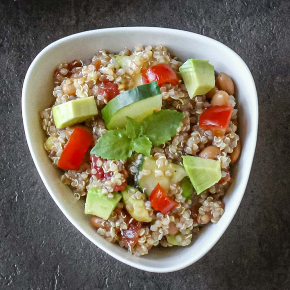 Overhead shot of quinoa cucumber salad garnished with basil leaves in a white bowl.