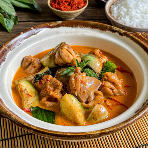 Close-up of Thai red curry with chicken and vegetables in a clay bowl.