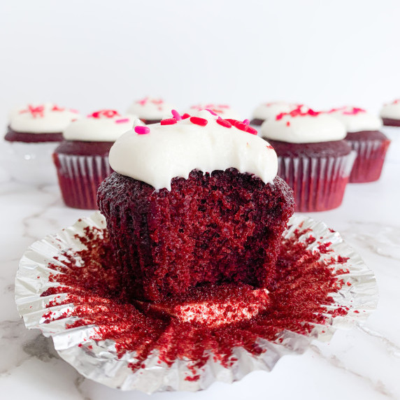 Red velvet cupcake on a wrapper with a bite taken out of it on a white counter