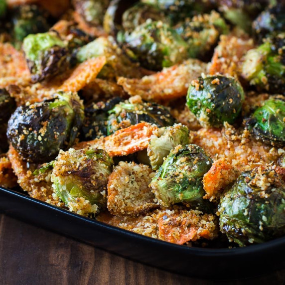 Side close up shot of roasted Brussel sprouts and carrots on a black plate on a dark wooden surface.