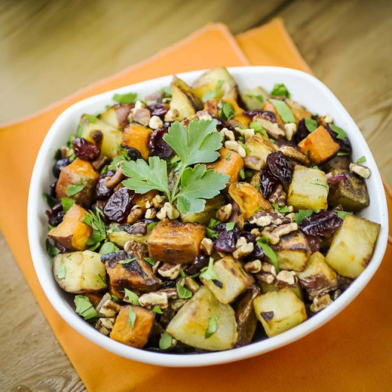 Overhead shot of potato medley garnished with parsley in a white bowl on an orange cloth.