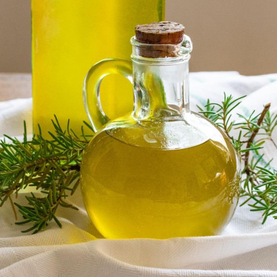oil inside a cruet with rosemary around it, standing on a white towel