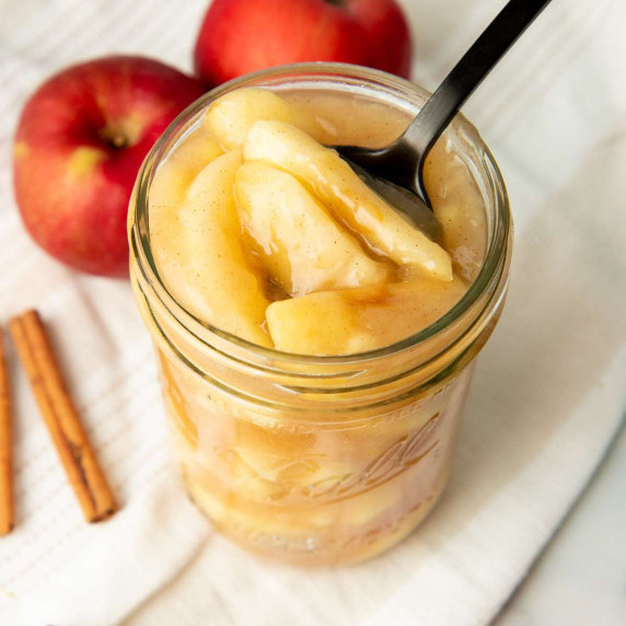 Top view of a spoon scooping homemade apple pie filling out of a glass canning jar.