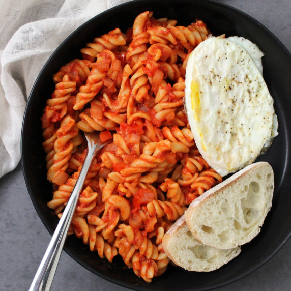 A bowl of shakshuka pasta noodles with a fried egg and bread on the side