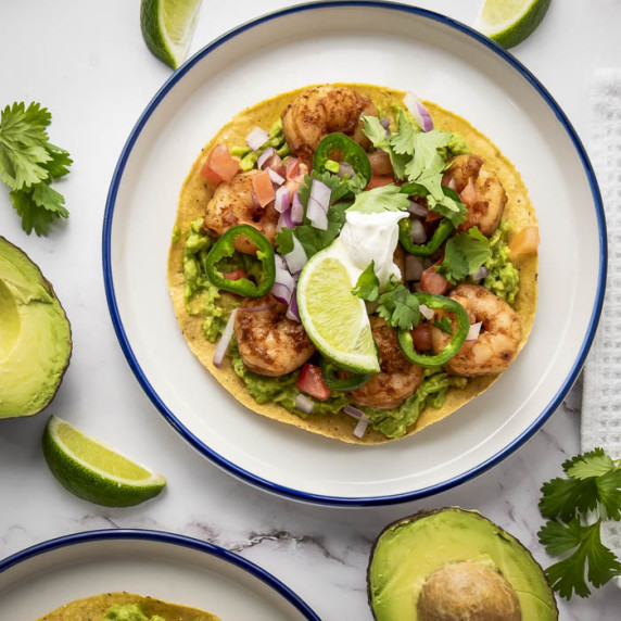 Overhead shot of two white and blue plates with shrimp tostadas garnished with fresh cilantro.