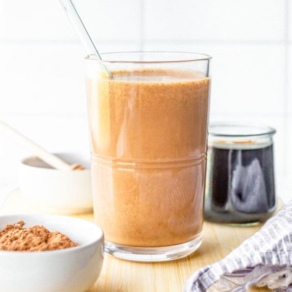 Chocolate coffee smoothie in a glass with a glass straw on a wooden cutting board.