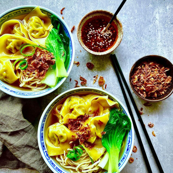 bowls of wonton noodle soup with chopsticks and condiments