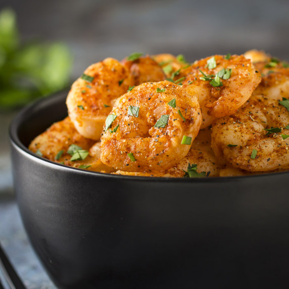 Side shot of shrimp garnished with fresh parsley in a black bowl with more herbs on the side.