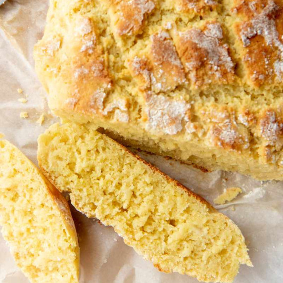 A round loaf of crusty gluten-free bread with two slices in front of it resting on parchment paper.
