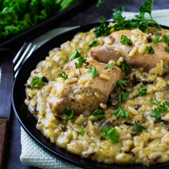 Side view of chicken and rice on a black plate garnished with herbs with silverware on the side.