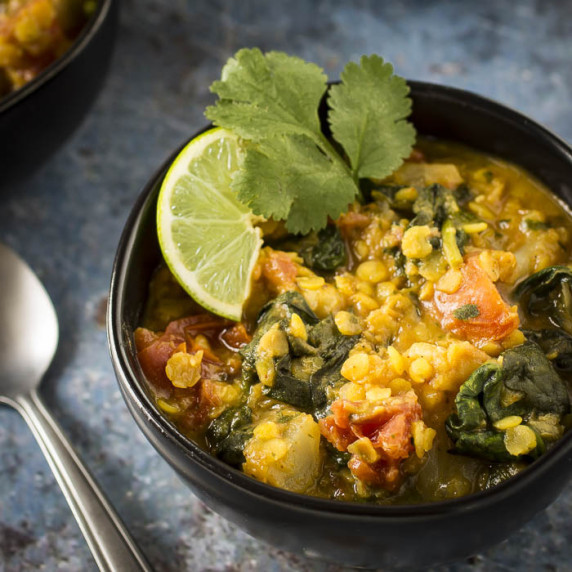 Angled close up shot of red lentil stew in a black bowl garnished with lime and cilantro.