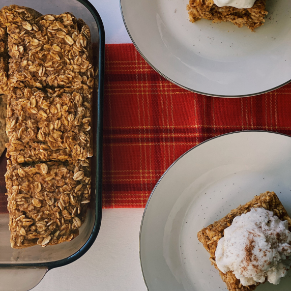 Dish of pumpkin baked oats and two white circle plates with portions topped with greek yogurt