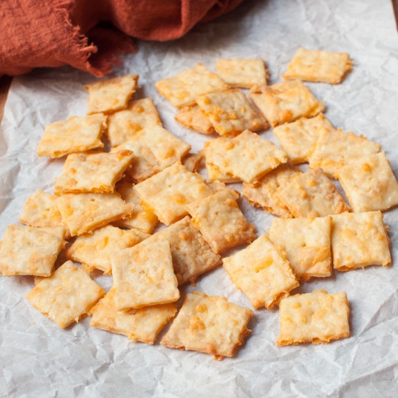 Sourdough cheese it crackers on a white background with an orange linen behind them. 