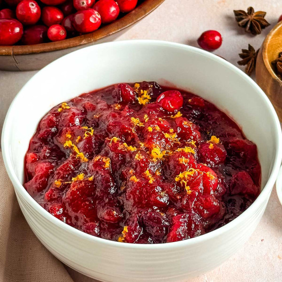 A white bowl of cranberry sauce next to a bowl of cranberries and star anise pods.