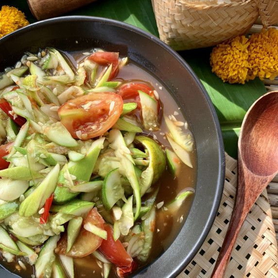 Top-view of spicy Lao cucumber salad with tomatoes in a black dish.
